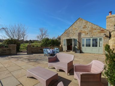 An outdoor patio with wicker furniture and a dining table outside a stone building at Roding Cottage in Egton