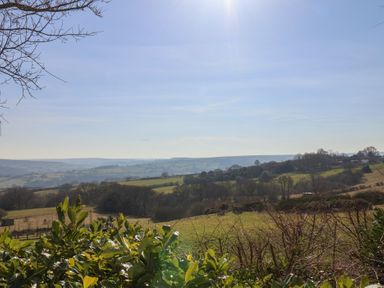 A countryside landscape with green fields trees and hills under a clear sky at Roding Cottage in Egton