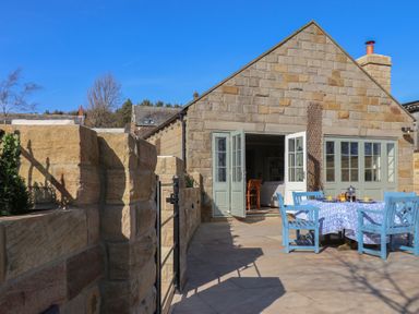 An outdoor patio area with a stone wall a blue table and chairs and an open door to a stone house at Roding Cottage in Egton