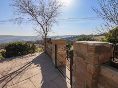 A stone patio with a metal gate and stone pillars overlooking a countryside landscape at Roding Cottage in Egton