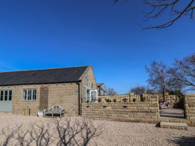 A stone building with a bench outside next to a stone wall and a gated patio area at Roding Cottage in Egton