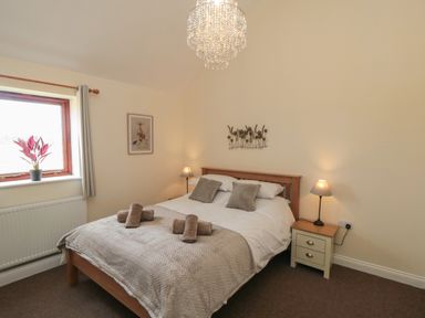A bedroom with a wooden bed a bedside table with a lamp a window and a plant on the windowsill at Curlew Cottage near Filey