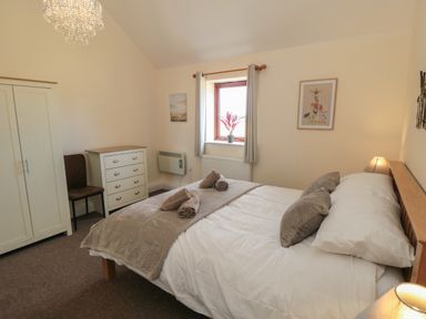 A bedroom with a bed with pillows and towels a wardrobe a chest of drawers a chair and a window at Curlew Cottage near Filey
