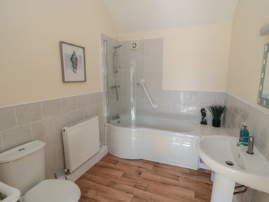 A bathroom with a bathtub shower combination toilet sink radiator and wall art at Curlew Cottage near Filey