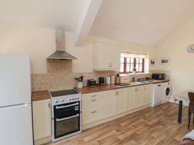 A kitchen with white cabinets wooden countertops a stove refrigerator dishwasher washing machine and a window at Curlew Cottage near Filey