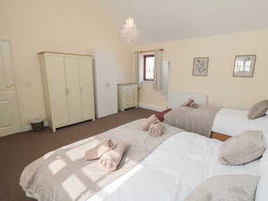 A bedroom with two beds a wardrobe a chest of drawers and a window at Curlew Cottage near Filey