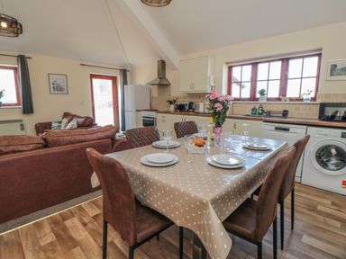 A kitchen and dining area with a table set for four people with chairs and a living area with sofas near Curlew Cottage near Filey