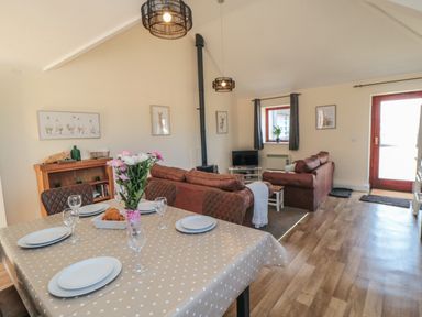 A dining table with plates and glasses and a vase with flowers next to a living room with sofas a TV and wood stove at Curlew Cottage near Filey