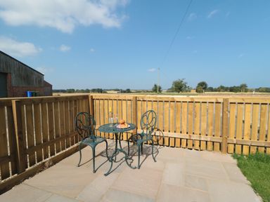 An outdoor patio with a metal table and two chairs a bottle of wine and glasses on the table at Curlew Cottage near Filey