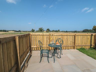 A patio area with a metal table and two chairs with a bottle and glasses on the table at Curlew Cottage near Filey