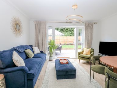 A living room with a blue sofa green armchairs a wall mirror and a round dining table at Pine Cottage in Wrentham