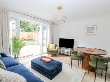A living room with blue sofa green armchair round dining table and open patio doors at Pine Cottage in Wrentham