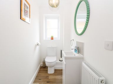 A small bathroom with a toilet a sink a round green mirror a radiator and a framed picture on the wall at Pine Cottage in Wrentham