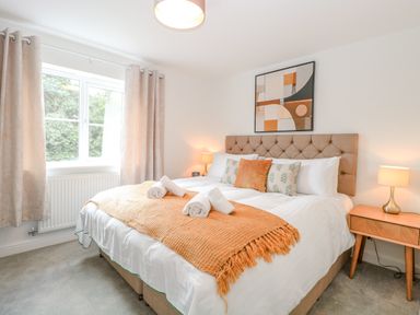 A bedroom with a large bed a headboard bedside tables lamps and a window at Pine Cottage in Wrentham