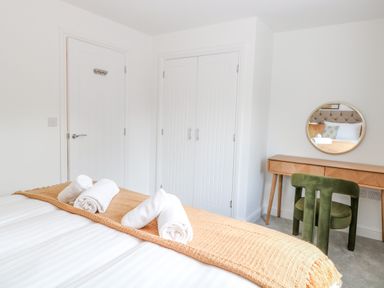A bedroom with a bed with rolled towels on a blanket a wooden desk with round mirror and green chair at Pine Cottage in Wrentham