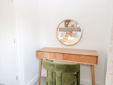A wooden desk with drawers and a round mirror above it with a green chair in front at Pine Cottage in Wrentham