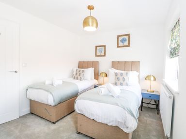 A bedroom with two single beds bedside tables lamps framed pictures and a window at Pine Cottage in Wrentham