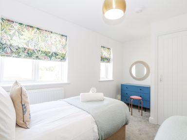 A bedroom with a bed, floral window blinds, blue dresser, round mirror, and a stool at Pine Cottage in Wrentham