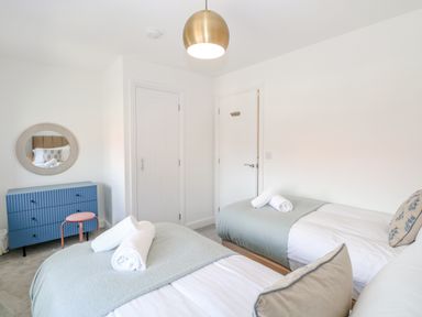 A bedroom with two single beds a blue dresser a round mirror and a gold ceiling light at Pine Cottage in Wrentham
