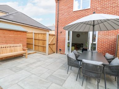A patio area with a table and chairs under an umbrella next to a wooden bench and storage shed at Pine Cottage in Wrentham