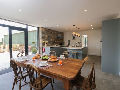 A kitchen and dining area with a wooden table set for breakfast and stone wall at The Hay Barn in Huntley