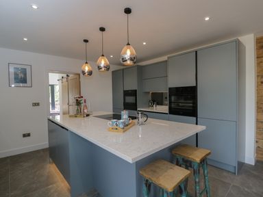 A kitchen with a large island table bar stools pendant lights and built in cabinets at The Hay Barn in Huntley