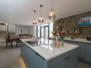 A kitchen with an island countertop with flowers and a bottle on it and a dining table with chairs at The Hay Barn in Huntley