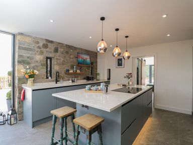 A kitchen with a stone wall and a marble countertop island with stools at The Hay Barn in Huntley