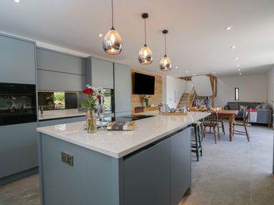 A kitchen with a large island countertop and dining table in the background at The Hay Barn in Huntley