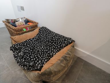 A pet bed with a black and white polka dot blanket and a wicker basket with pet bowls and treats on a tiled floor at The Hay Barn in Huntley