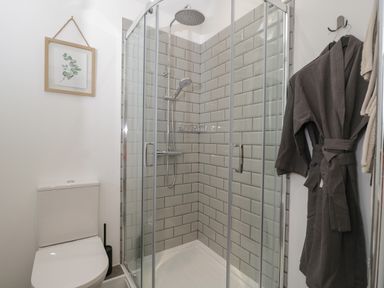 A bathroom with a shower enclosure tiled with rectangular tiles a toilet and a hanging grey robe at The Hay Barn in Huntley