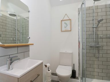 A bathroom with a sink, toilet, shower, mirror, and framed picture at The Hay Barn in Huntley