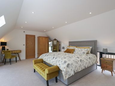 A bedroom with a bed a wooden wardrobe a desk with chair and a bench at The Hay Barn in Huntley