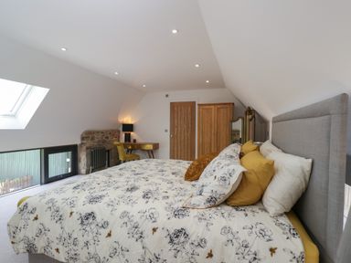 A bedroom with a bed with floral bedding a wooden wardrobe a desk with a chair and a mirror at The Hay Barn in Huntley