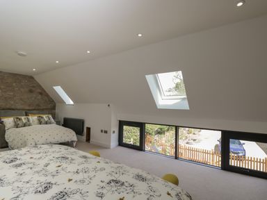 A bedroom with two beds a stone wall and windows on slanted ceilings at The Hay Barn in Huntley