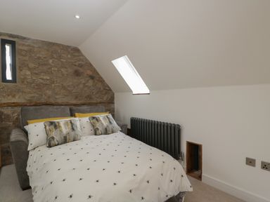 A bedroom with a bed against a stone wall under a skylight window and a radiator on the opposite wall at The Hay Barn in Huntley