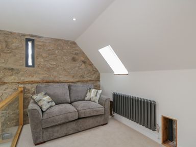 A gray sofa with two cushions near a stone wall and a radiator under a skylight at The Hay Barn in Huntley