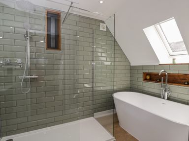 A bathroom with a freestanding bathtub and a glass shower enclosure with tiled walls and a skylight window at The Hay Barn in Huntley