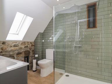 A bathroom with a shower, toilet, sink, skylight window, and stone and tile walls at The Hay Barn in Huntley