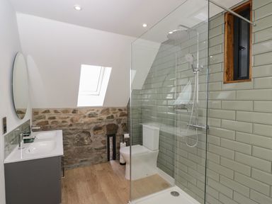 A bathroom with double sink vanity toilet glass shower and stone wall at The Hay Barn in Huntley