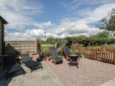 An outdoor patio area with black lounge chairs and wooden chairs around a small fire pit at The Hay Barn in Huntley