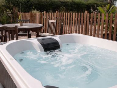 An outdoor hot tub with bubbling water next to a wooden table and chairs by a wooden fence at The Hay Barn in Huntley