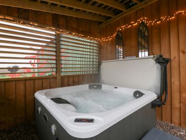 A hot tub in a wooden structure with lights at The Hay Barn in Huntley