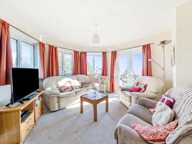 A living room with leather sofas a wooden coffee table a television on a wooden stand and red curtains at Bayview in Overcombe near Preston