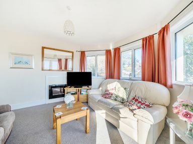 A living room with a white leather sofa pink curtains a wooden coffee table and a television at Bayview in Overcombe near Preston