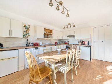 A kitchen with a wooden dining table and chairs white cabinets appliances and a decorative gecko on the wall at Bayview Overcombe near Preston