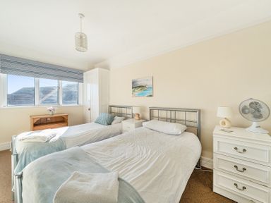 A bedroom with two single beds a window a wooden table and white drawers at Bayview in Overcombe near Preston