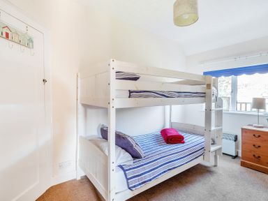 A bedroom with a white bunk bed with striped bedding and a red towel a wooden chest of drawers and a window with a blue blind at Bayview in Overcombe near Preston
