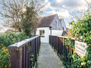 A narrow pathway with wooden railings leading to a small building with tiled roofs at Bayview Overcombe near Preston
