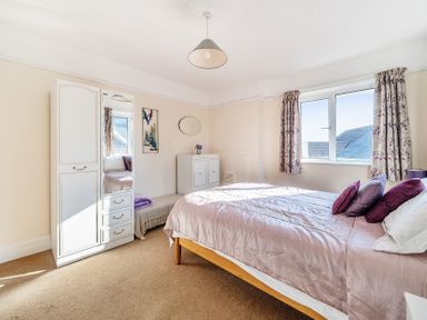 A bedroom with a bed pillows a wardrobe bench cabinet and window with curtains at Bayview in Overcombe near Preston